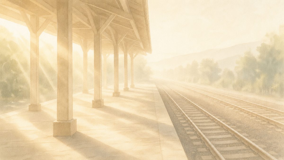 朝日が斜めに差し込む早朝の無人の駅ホームと遠くへ霞む線路。毎日の通勤と、そこから踏み出す一歩のイメージ