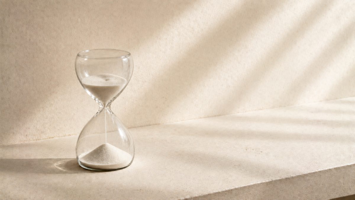 朝の光が差す石の天板に置かれたガラスの砂時計 — 時間と集中力の掛け算を表すイメージ
